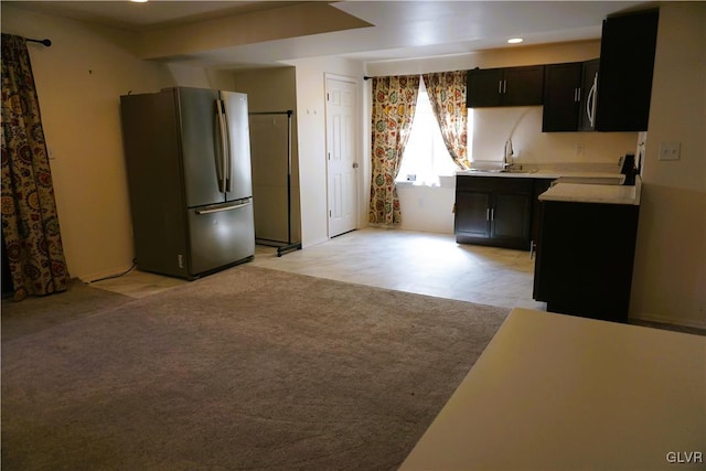 kitchen with a sink, light colored carpet, light countertops, freestanding refrigerator, and dark cabinets