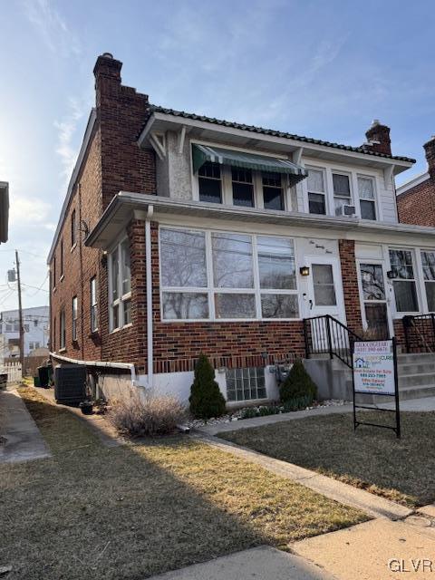 view of front facade with brick siding, central AC unit, and a chimney