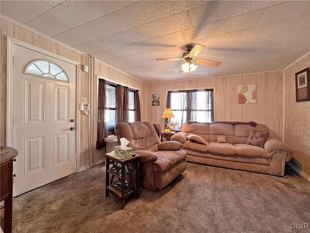 carpeted living area featuring wooden walls, crown molding, and ceiling fan