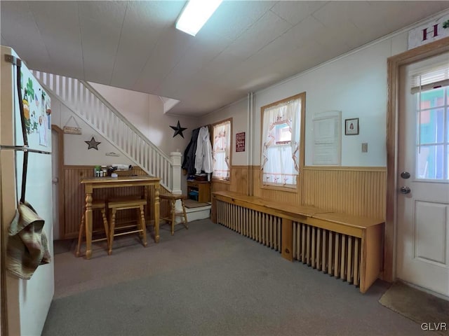 entryway with stairs, a wainscoted wall, wood walls, and carpet flooring