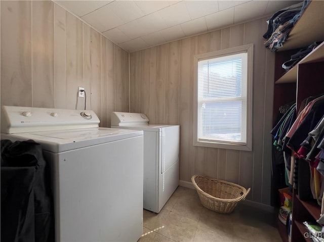 clothes washing area featuring light tile patterned floors, wooden walls, separate washer and dryer, and laundry area