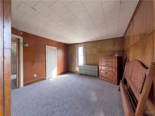 unfurnished bedroom with wood walls, radiator, and carpet floors