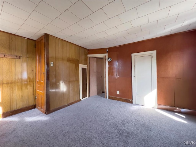 carpeted spare room featuring wooden walls