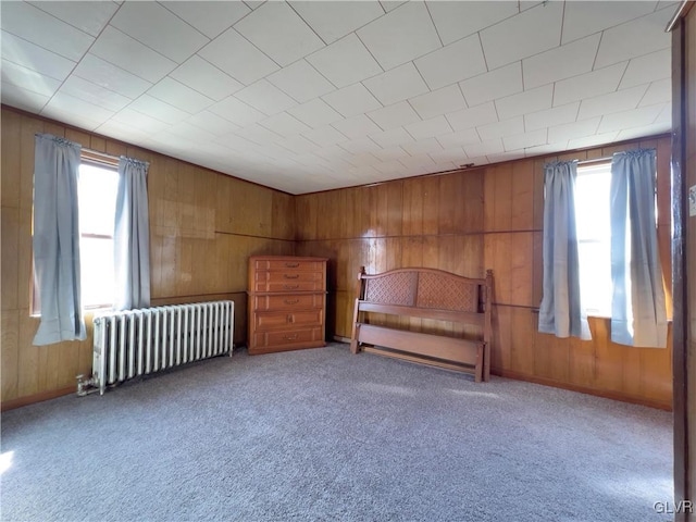 unfurnished bedroom with multiple windows, radiator, wood walls, and carpet