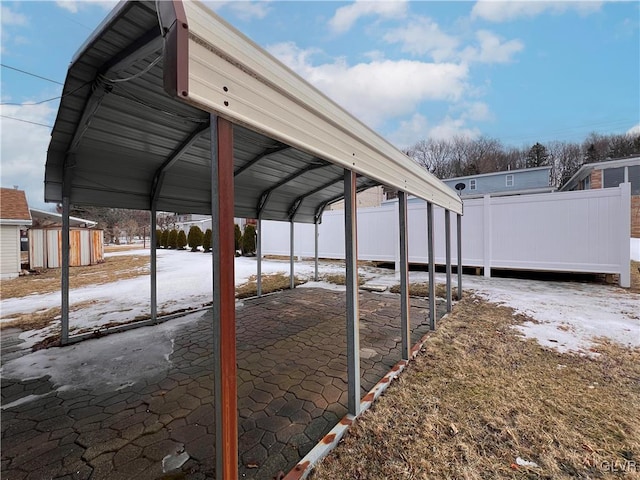 snow covered patio featuring a carport, a storage unit, an outbuilding, and fence