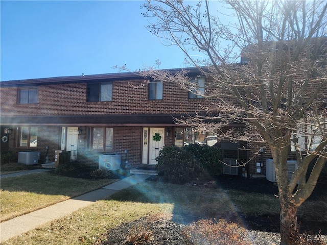 view of property with a front lawn, central AC unit, and brick siding