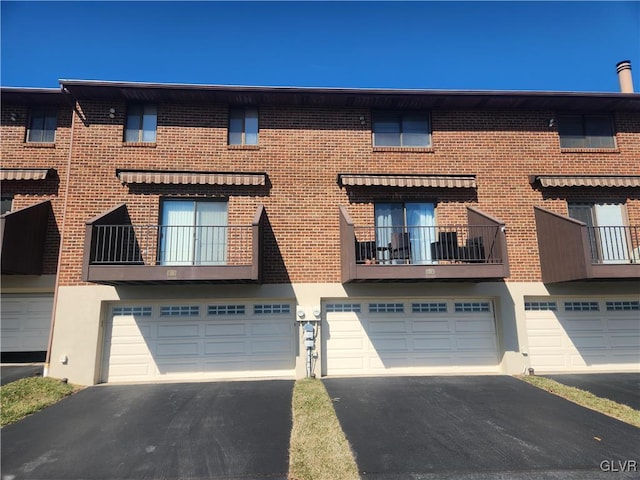 multi unit property featuring an attached garage, brick siding, and driveway