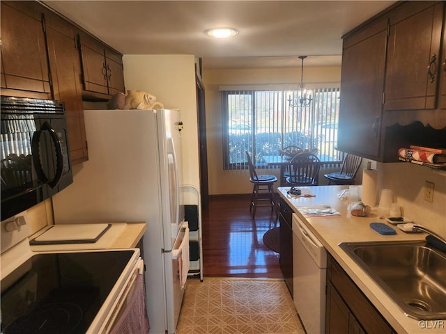 kitchen featuring dark brown cabinets, light countertops, a notable chandelier, white appliances, and a sink