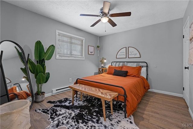 bedroom with a textured ceiling, a baseboard heating unit, baseboards, and wood finished floors