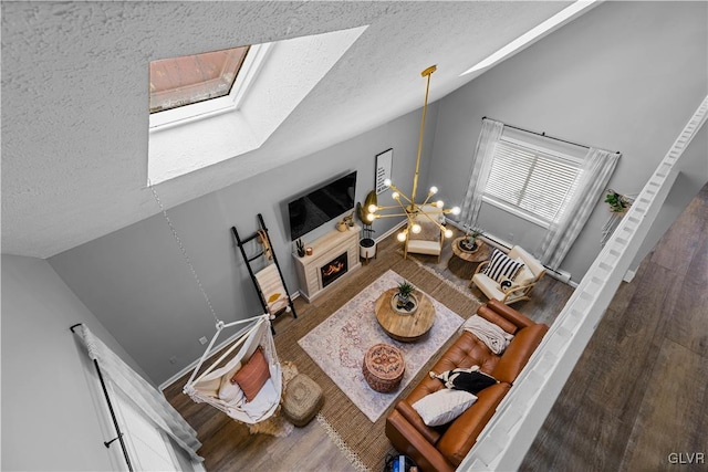 living room with vaulted ceiling with skylight, wood finished floors, a lit fireplace, and a textured ceiling