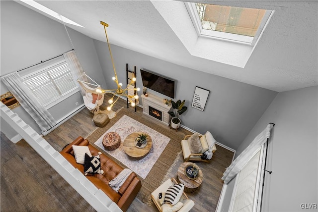 living room featuring baseboards, lofted ceiling with skylight, a chandelier, wood finished floors, and a textured ceiling