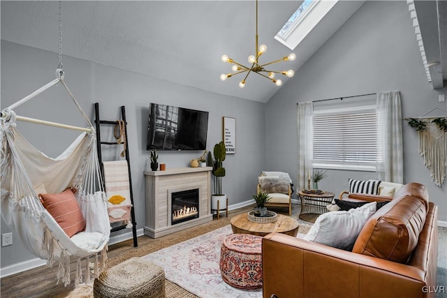 living room featuring a chandelier, a skylight, wood finished floors, a glass covered fireplace, and high vaulted ceiling