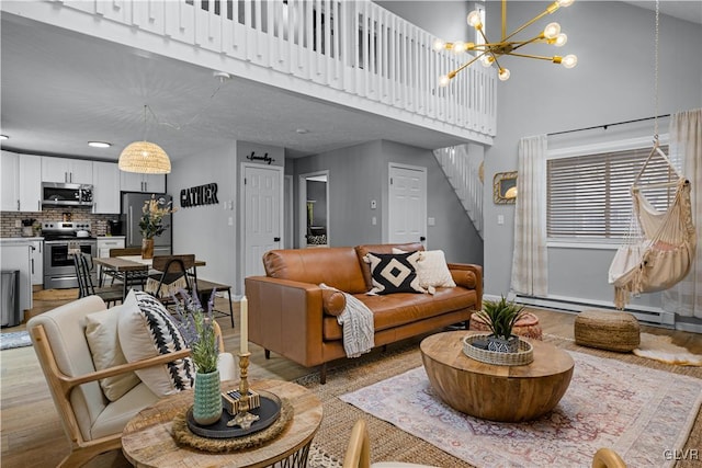 living room featuring stairway, light wood-type flooring, a towering ceiling, an inviting chandelier, and a baseboard radiator