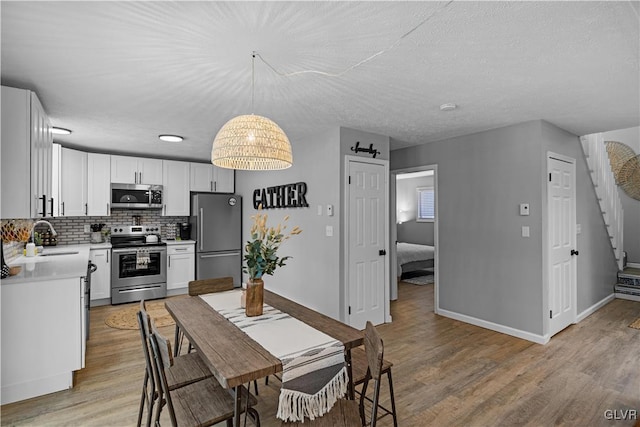 dining space featuring stairway, baseboards, a textured ceiling, and light wood-style flooring