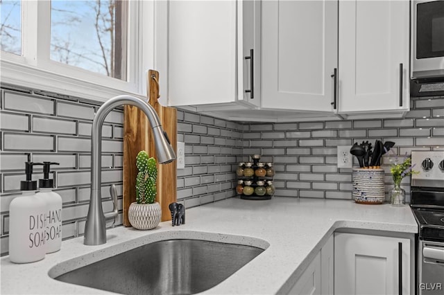 kitchen featuring white cabinets, backsplash, appliances with stainless steel finishes, and a sink