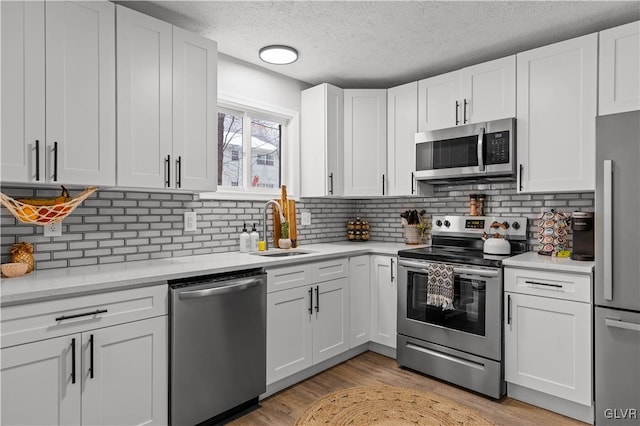 kitchen with light wood-type flooring, a sink, appliances with stainless steel finishes, white cabinetry, and tasteful backsplash