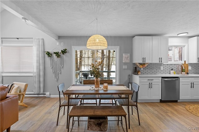 dining area featuring light wood-type flooring, a baseboard radiator, and a textured ceiling