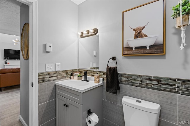 bathroom featuring toilet, tile walls, wainscoting, and vanity