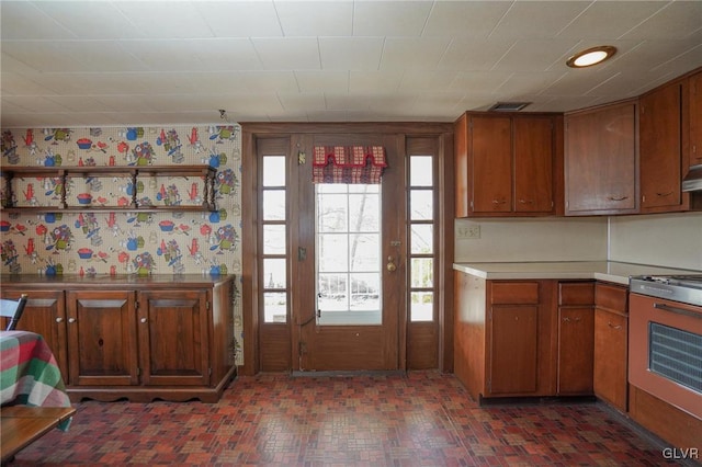 kitchen with visible vents, brown cabinets, wallpapered walls, range, and light countertops