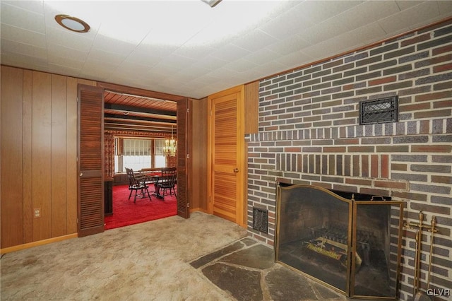 unfurnished living room with wooden walls, a fireplace, visible vents, and carpet floors