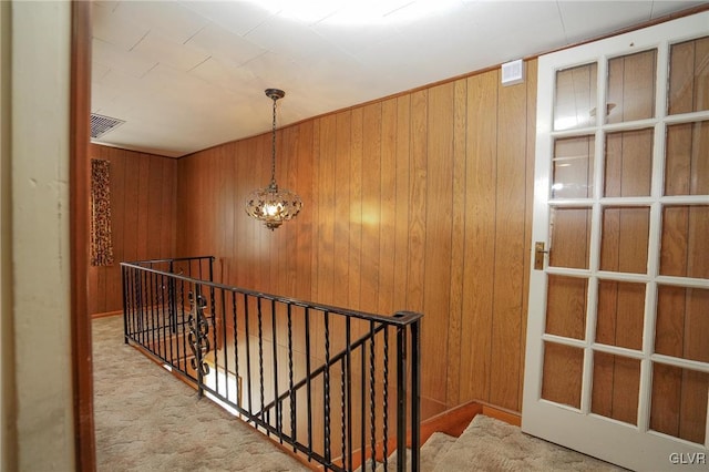 hall featuring wooden walls, an upstairs landing, and visible vents