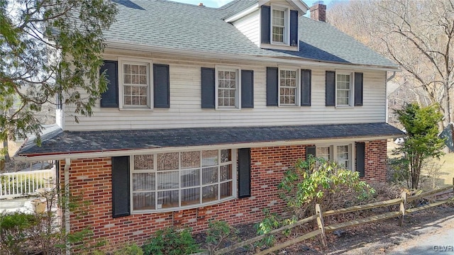 view of front of home featuring brick siding, roof with shingles, and a chimney