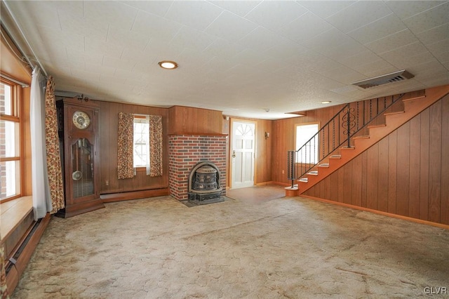 unfurnished living room featuring carpet, visible vents, a baseboard radiator, a wood stove, and stairs