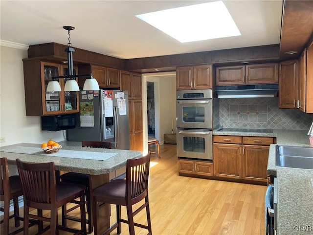 kitchen with stainless steel appliances, light countertops, light wood-style floors, under cabinet range hood, and backsplash