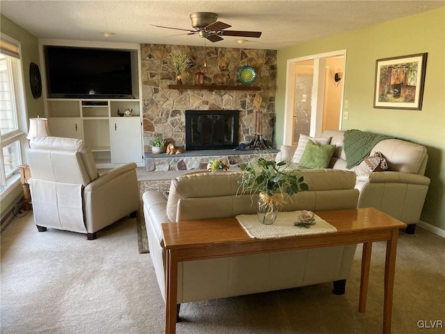 living area featuring a ceiling fan, baseboards, a stone fireplace, a textured ceiling, and carpet flooring