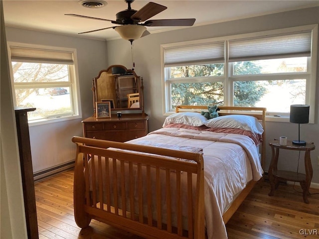 bedroom featuring a baseboard heating unit, visible vents, a ceiling fan, and light wood finished floors