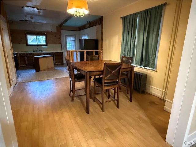 dining space with radiator, light wood-style floors, and baseboards