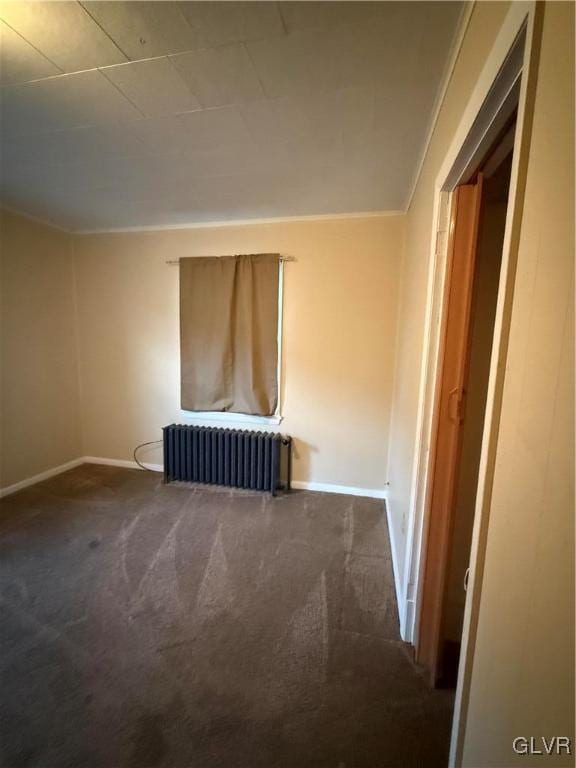 carpeted empty room featuring radiator and baseboards