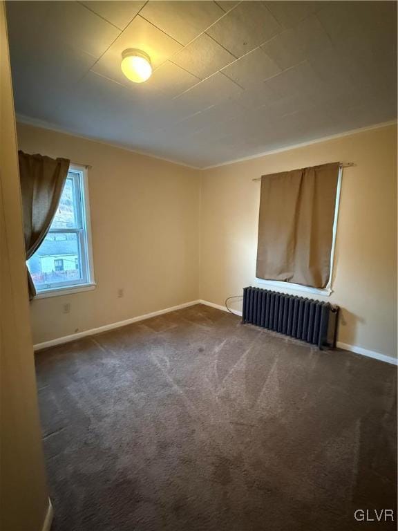 unfurnished room with baseboards, dark carpet, and radiator heating unit