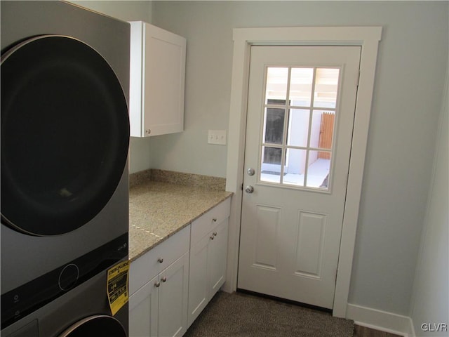 washroom with cabinet space, baseboards, and stacked washing maching and dryer