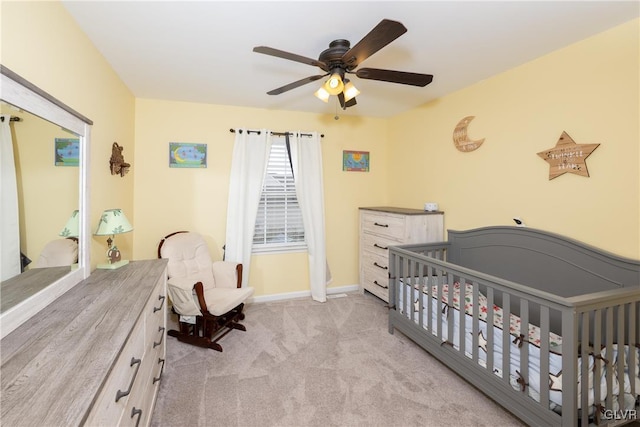 bedroom with a crib, light colored carpet, baseboards, and ceiling fan