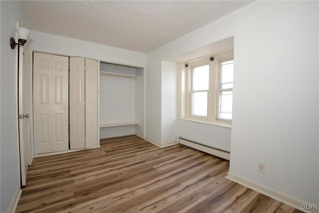 unfurnished bedroom with a closet, baseboards, baseboard heating, and wood finished floors