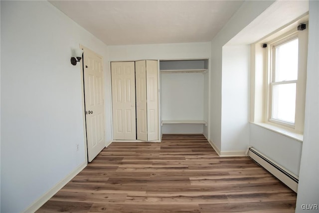 unfurnished bedroom with a closet, baseboard heating, baseboards, and wood finished floors