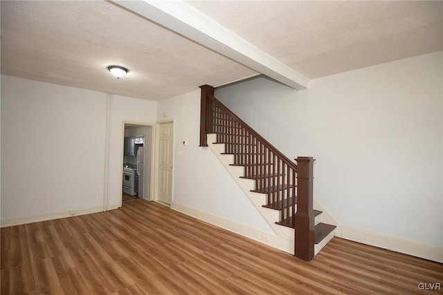 staircase with wood finished floors, baseboards, and a textured ceiling