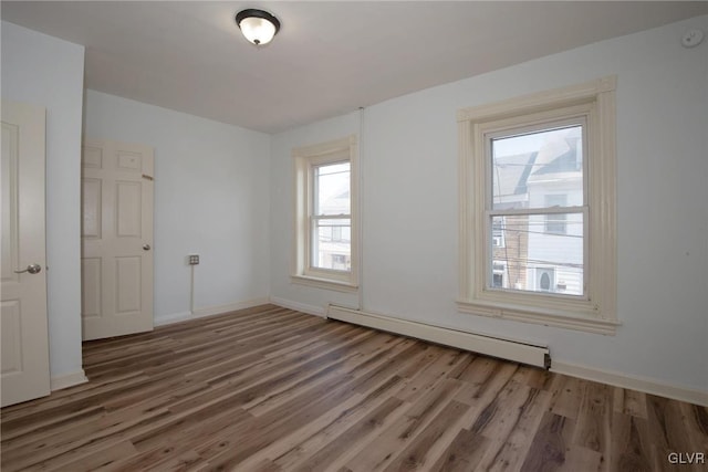 unfurnished room with a baseboard radiator, baseboards, and wood finished floors