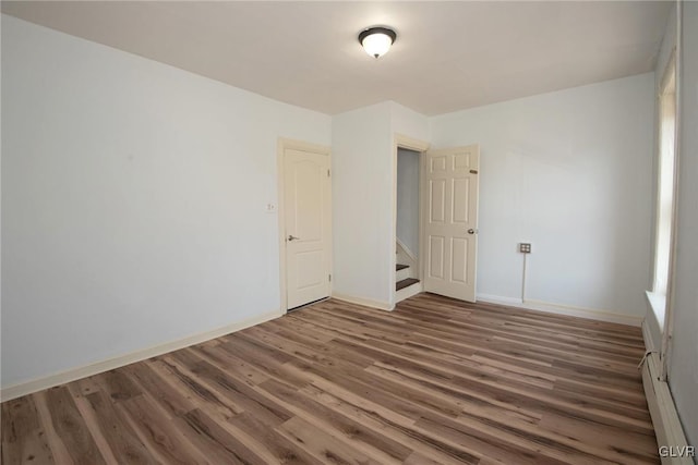 unfurnished room with wood finished floors, baseboards, and a baseboard radiator