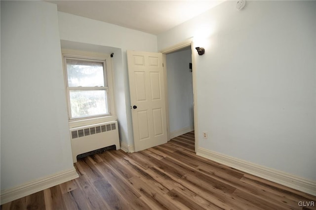 spare room featuring baseboards, wood finished floors, and radiator heating unit