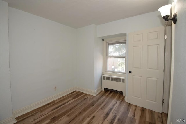 unfurnished room with radiator, wood finished floors, and baseboards