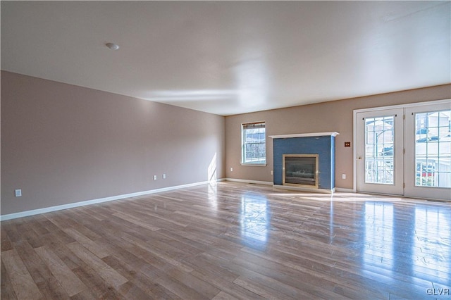 unfurnished living room featuring a glass covered fireplace, baseboards, and wood finished floors