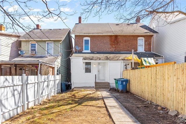 back of house featuring entry steps, a fenced backyard, brick siding, and a chimney