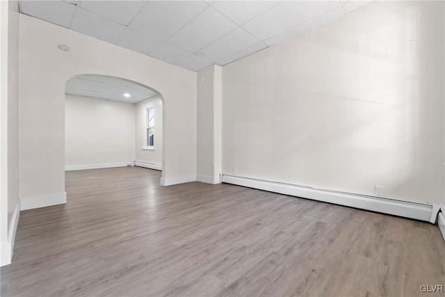 empty room with a paneled ceiling, a baseboard radiator, arched walkways, and wood finished floors