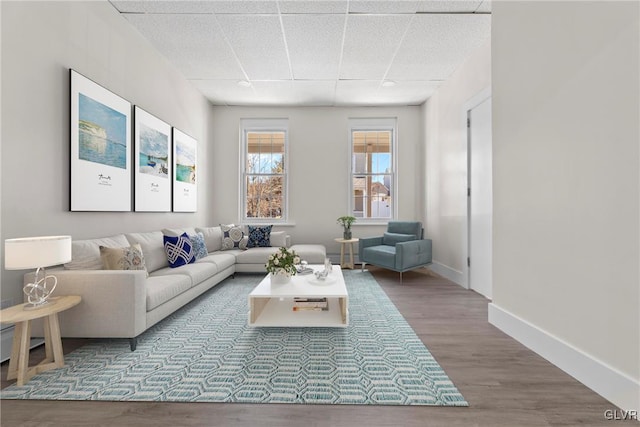 living room with a paneled ceiling, baseboards, and wood finished floors