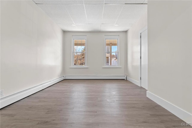 spare room with baseboard heating, wood finished floors, baseboards, and a drop ceiling