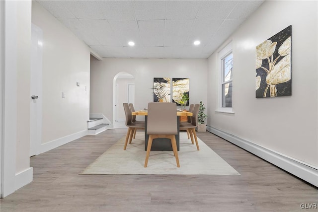 dining room with baseboards, a drop ceiling, baseboard heating, wood finished floors, and arched walkways