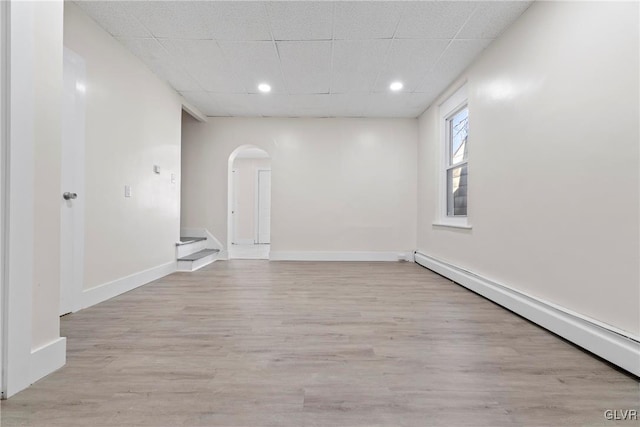 unfurnished room with baseboards, arched walkways, a drop ceiling, light wood-style floors, and baseboard heating