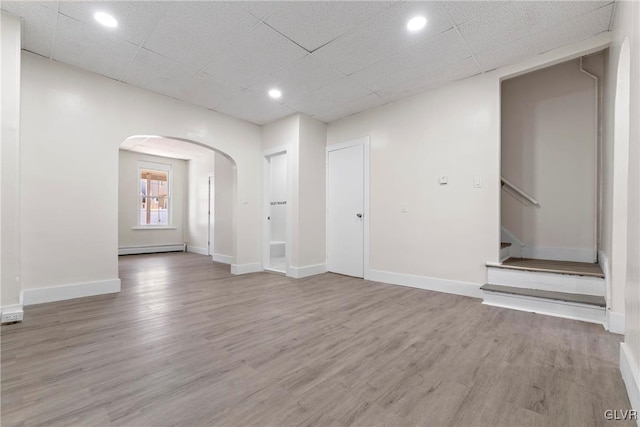 unfurnished living room with wood finished floors, arched walkways, baseboard heating, and baseboards